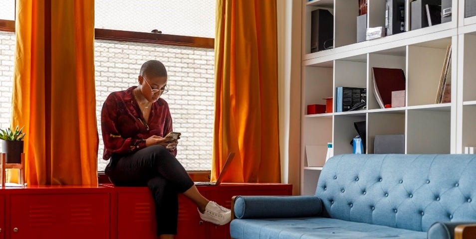 A young woman sitting cross legged on a cabinet looking at her phone.