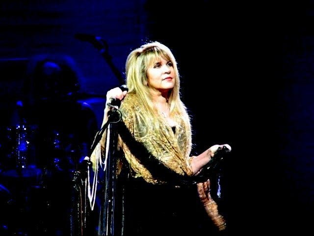 Singer Stevie Nicks wearing a gold shawl and holding a mic.