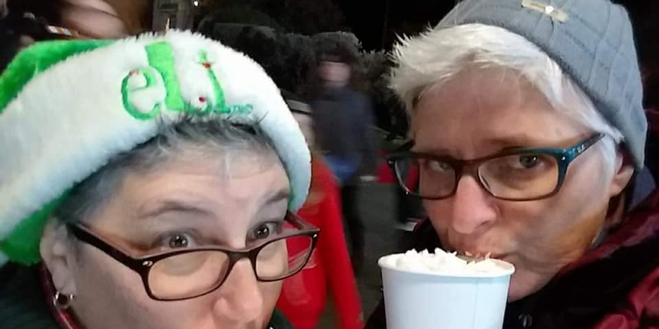 Two women, one in an elf hat, sipping hot chocolate