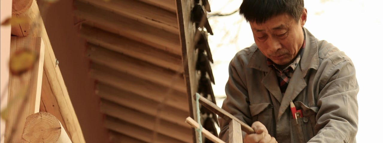 A man using a hand saw to cut a beam