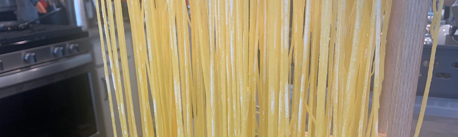 Homemade pasta hanging on a wooden drying rack in a kitchen.