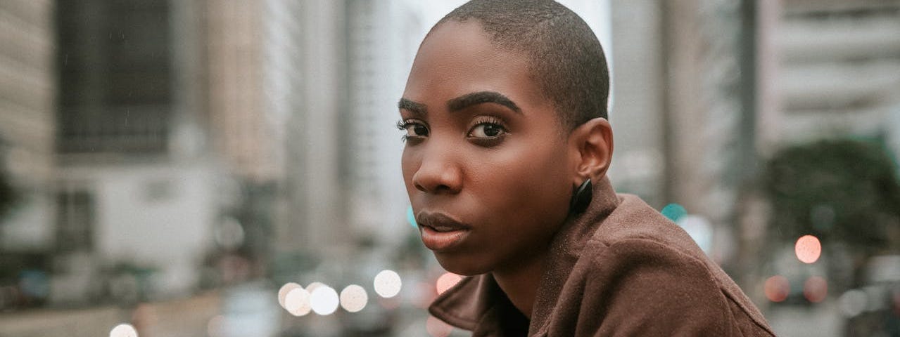 A beautiful Black woman with a shaved head looks out over a city street.