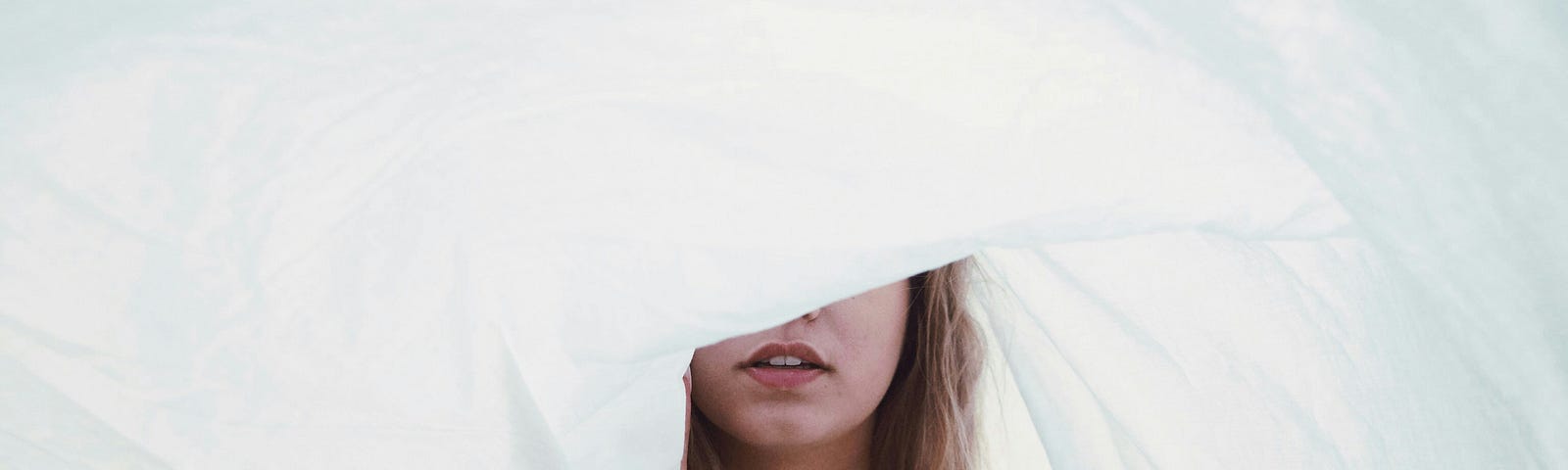 Teenage girl in white partially hiding her face behind a billowing white sheet