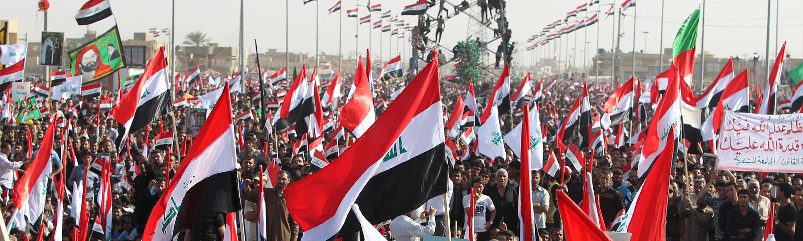 A large crowd holds up numerous Iraqi flags at a protest.