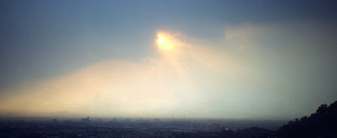 The valley of Mexico City with a dark cloud above and the sun partially shining opaquely through the clouds.