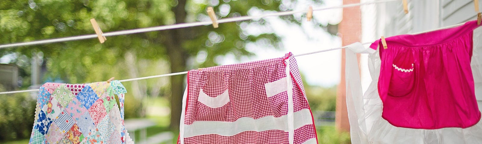 Three colorful aprons on a clothesline in a sunny yard.