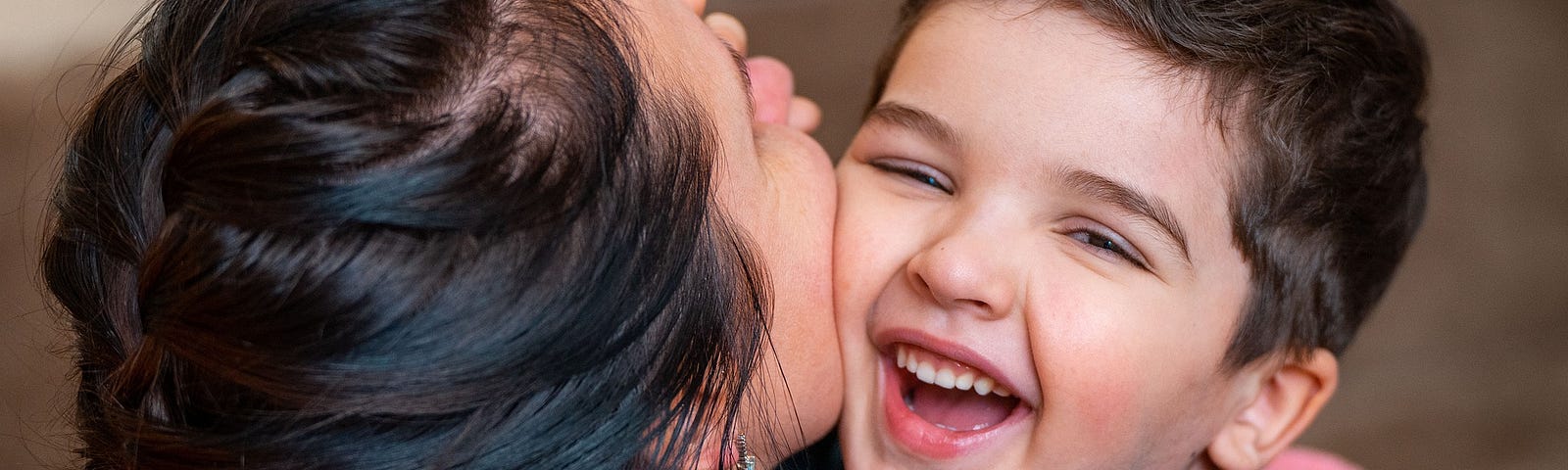 Mother holding laughing toddler boy as she kisses his cheek