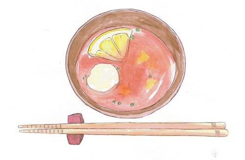 A bowl of reddish soup with a quartered lemon floating in it. A pair of wooden chopsticks are on a chopstick rest next to it.