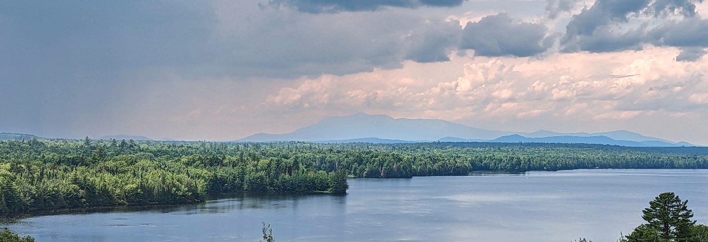 The view of a distant mountain is partially obscured by haze. A wilderness lake is in the foreground.