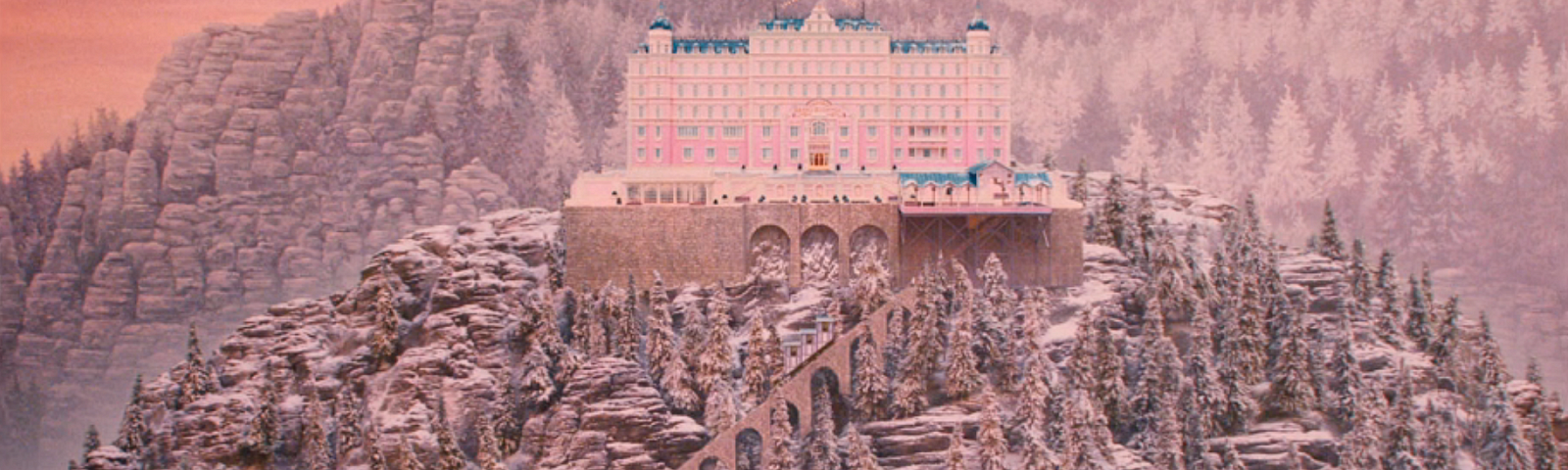 A lavish, pink hotel sits atop a tall, snowy mountain against a pink-er sky and tree-crested alps
