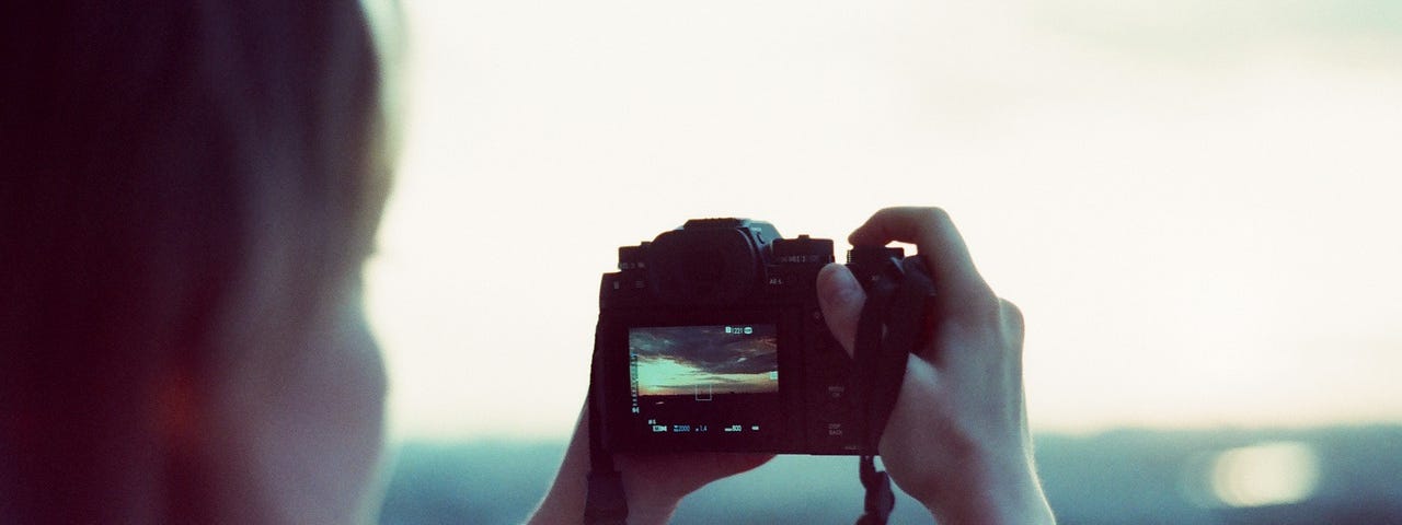 Girl taking a photo out her back window, using a dslr camera.