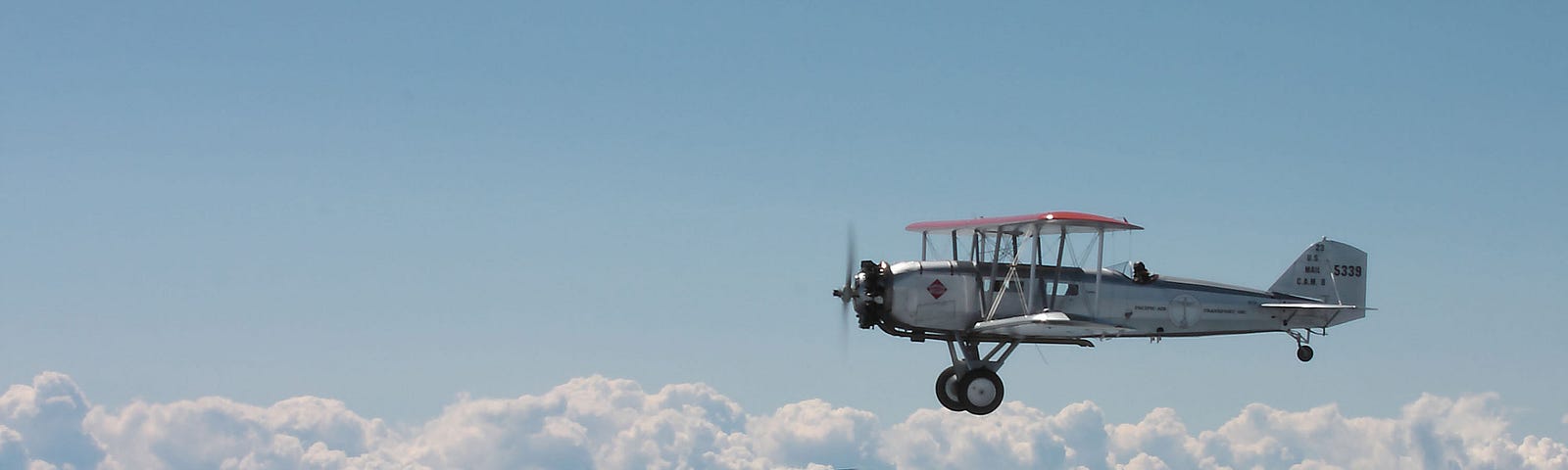 A modern jet and an old biplane flying above clouds