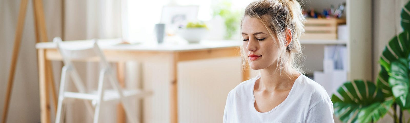 A young attractive woman in a white t-shirt in a clean office room meditating