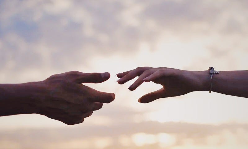 Couple reaching for each other to hold hands with a sunset behind them