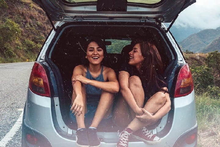 Picture of girls in car, could be sisters, enjoying each other’s company.