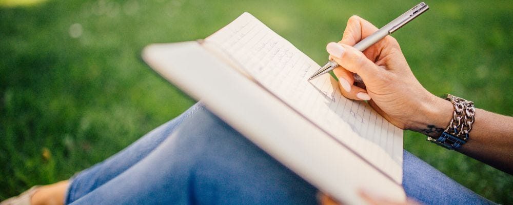 Woman’s hand holding pen writing on a tablet balanced on her knees.