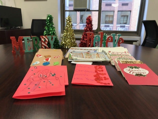 handmade cards laying on a table in the foreground. With two wood blocks that say “Merry” and “Believe” in the background.