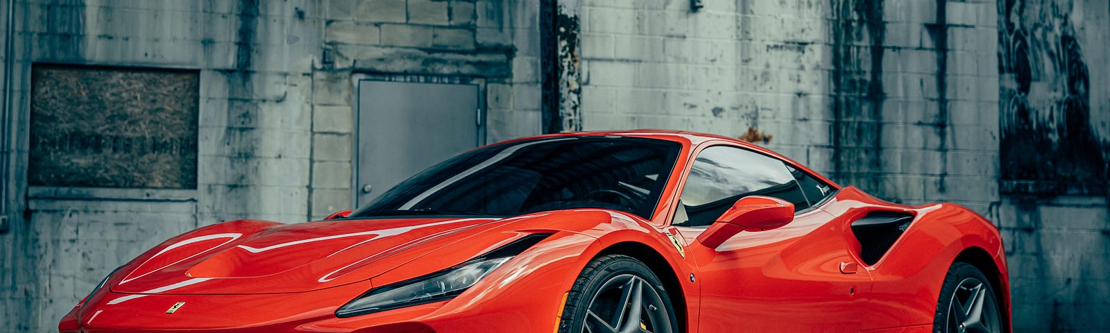 A red Ferrari parked in front of an old grey brick wall, likely in an old factory building.