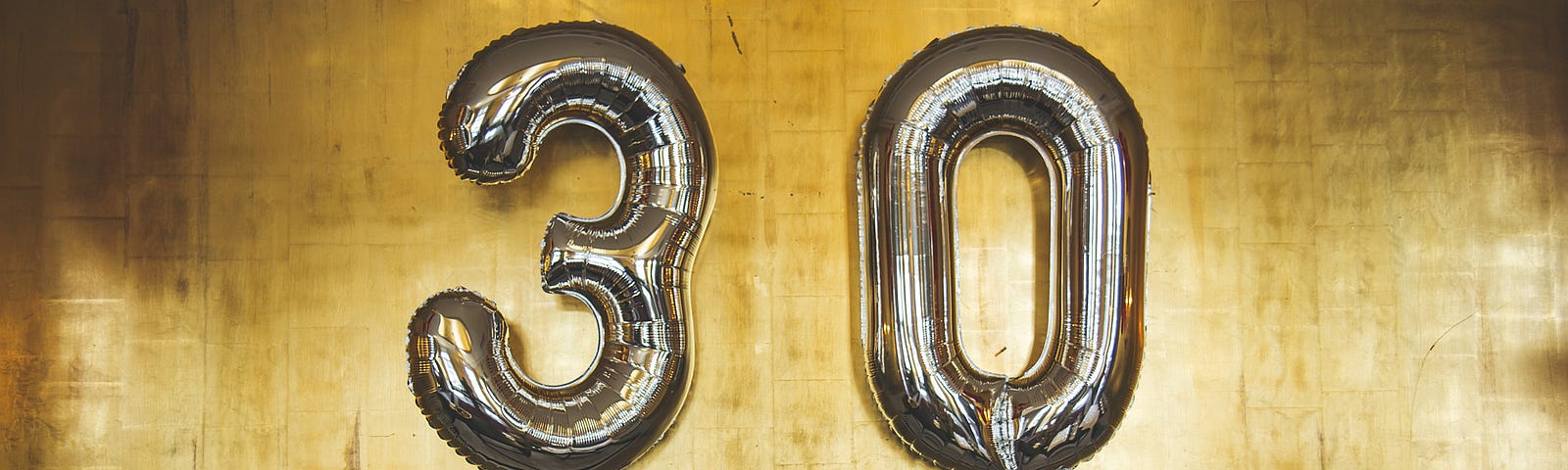 the number 30 in gold foil balloons against a yellow wall