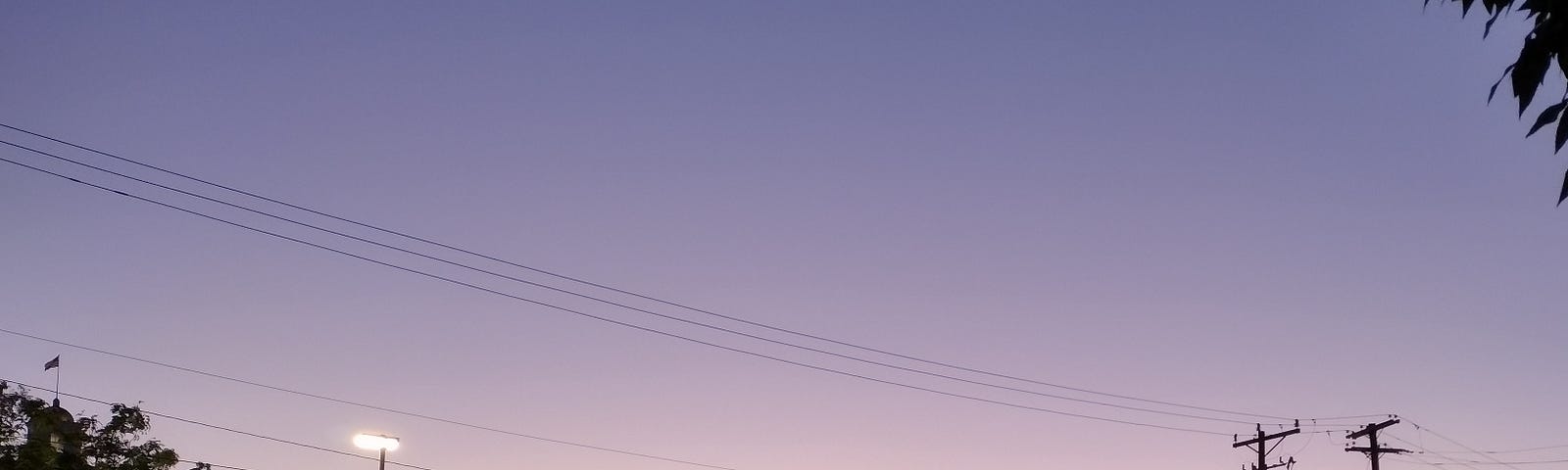 An automobile dealership with full flood lights on, in the light of the sun.