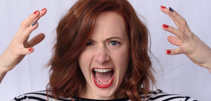 Close up of an angry red-haired woman with red lips, and open mouth with teeth bared.