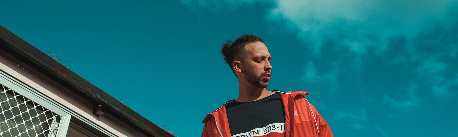 Flewnt wears a red jacket, looking away. Behind him is a clear, blue sky.