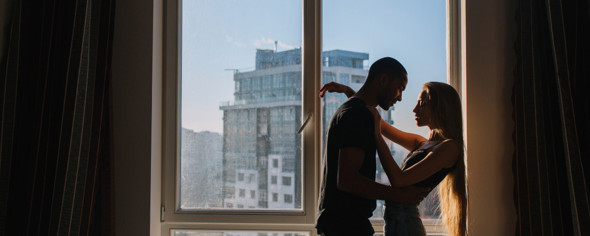 Couple holding each other in front of large window