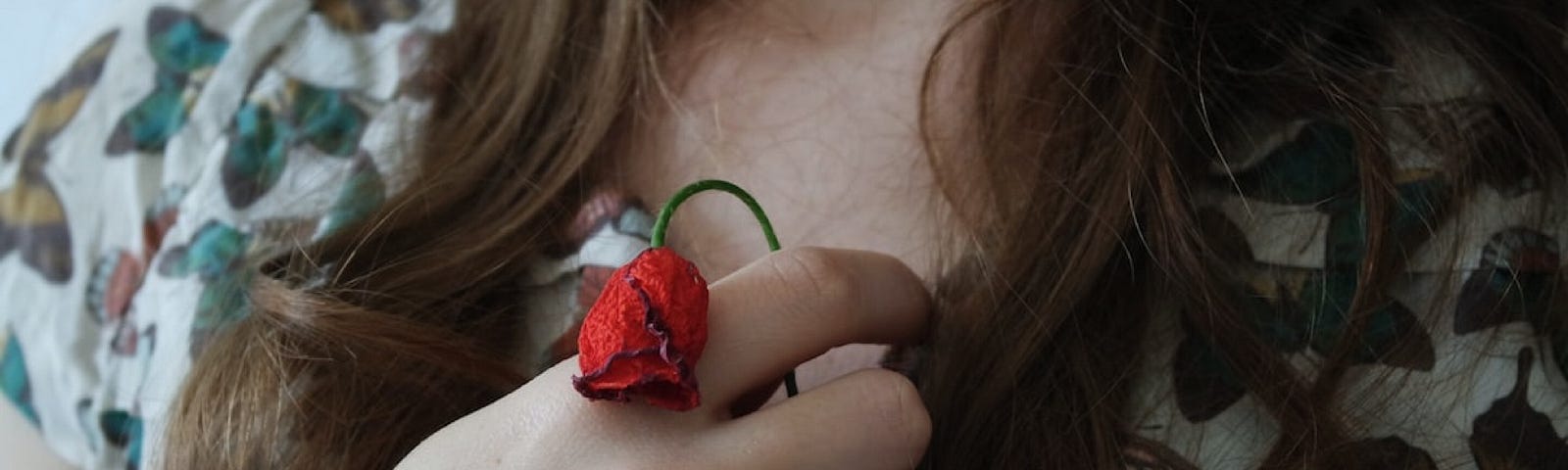 A woman holding a wilted poppy in front of her chest.
