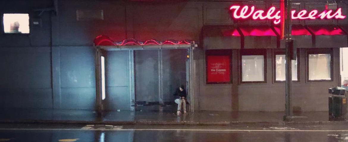 A lone boy sits on a bus stop bench texting on a cold, wet night in the Castro District of San Francisco.