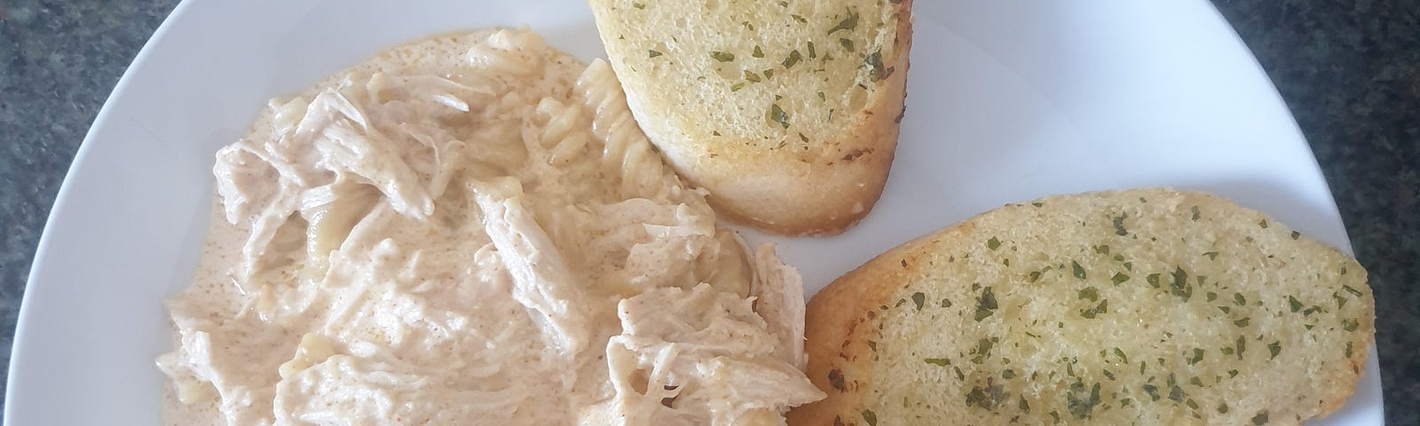 A plate of hicken Alfredo pasta with garlic bread