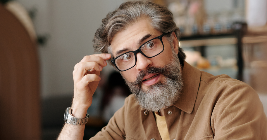 Business man wearing glasses. He also has a beard. And a watch. Some grey hair. He doesn’t look like me, I don’t have hair.