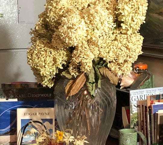 Old red kitchen table with a glass vase of dried limelight hydrangeas, books about art, and a coffee mug.