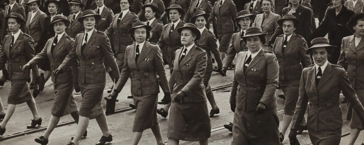 A black and white photo, from 1940, of a dozen or so stern-faced, middle-aged women marching in formation down a city street. They are wearing Australian army uniforms.