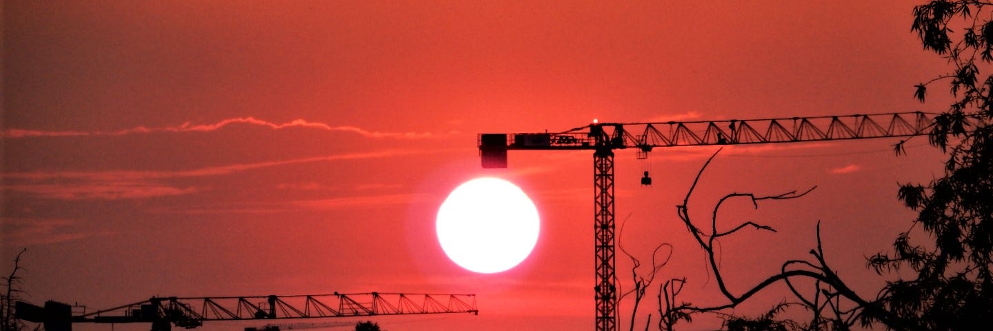 Red sunset. The orb of the sun sits below the cab of an industrial crane.