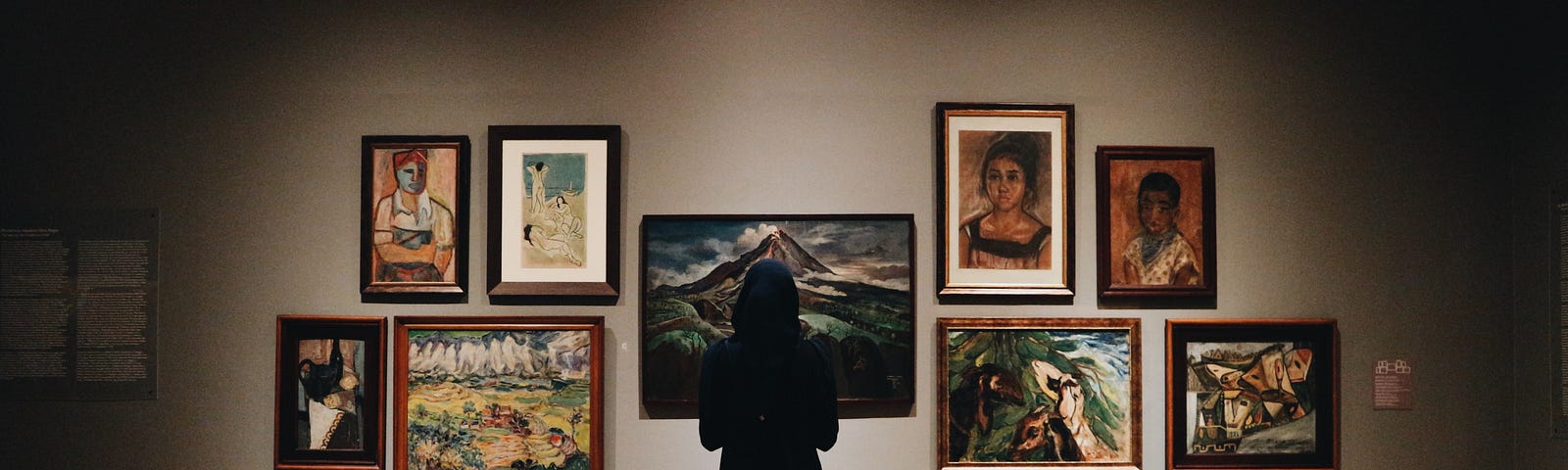 Person facing a wall of art in a softly lit art gallery
