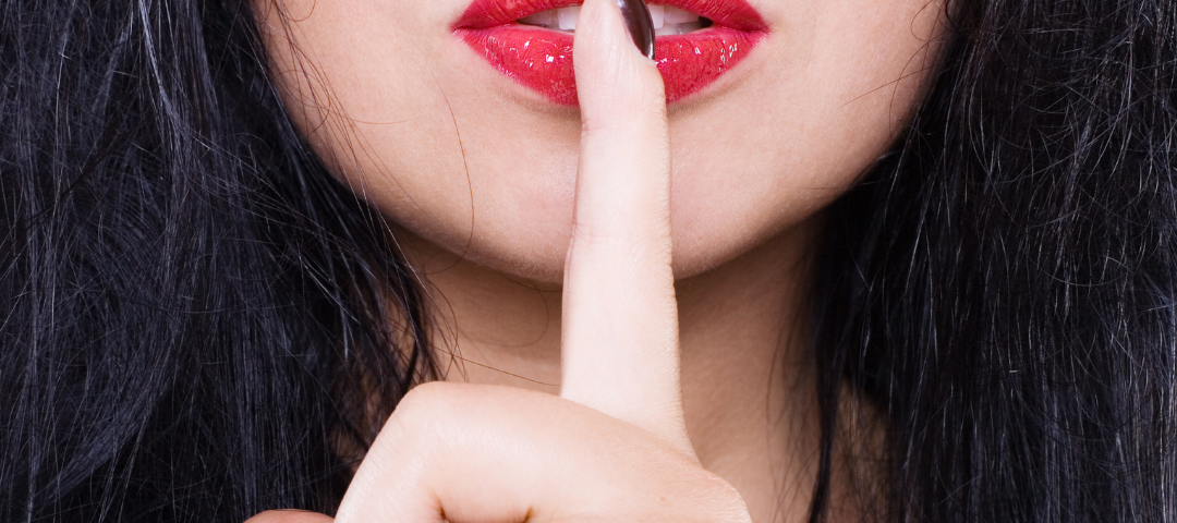 woman with red lipstick and dark hair with her finger to her lips