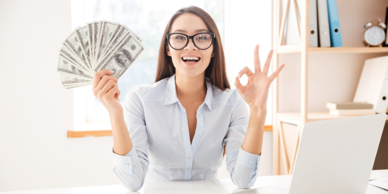 Woman holding up fanned cash — How I Make More By Writing Less