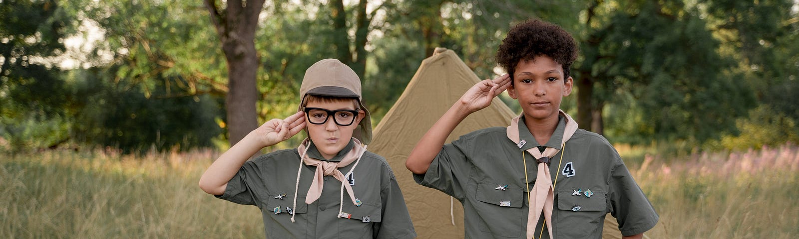 A photo of two boy scouts standing and saluting in front of their tent.