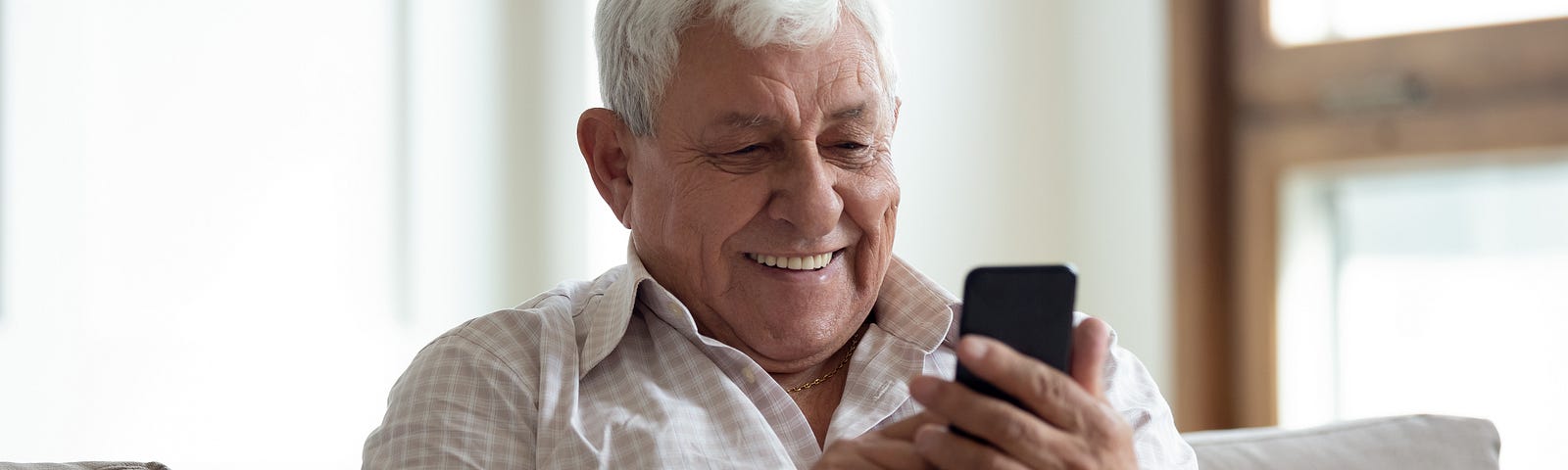 Older man smiles while reading off a cell phone screen.