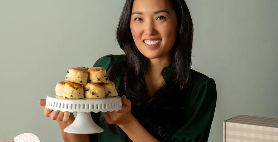 smiling woman holding a cake plate piled with scones