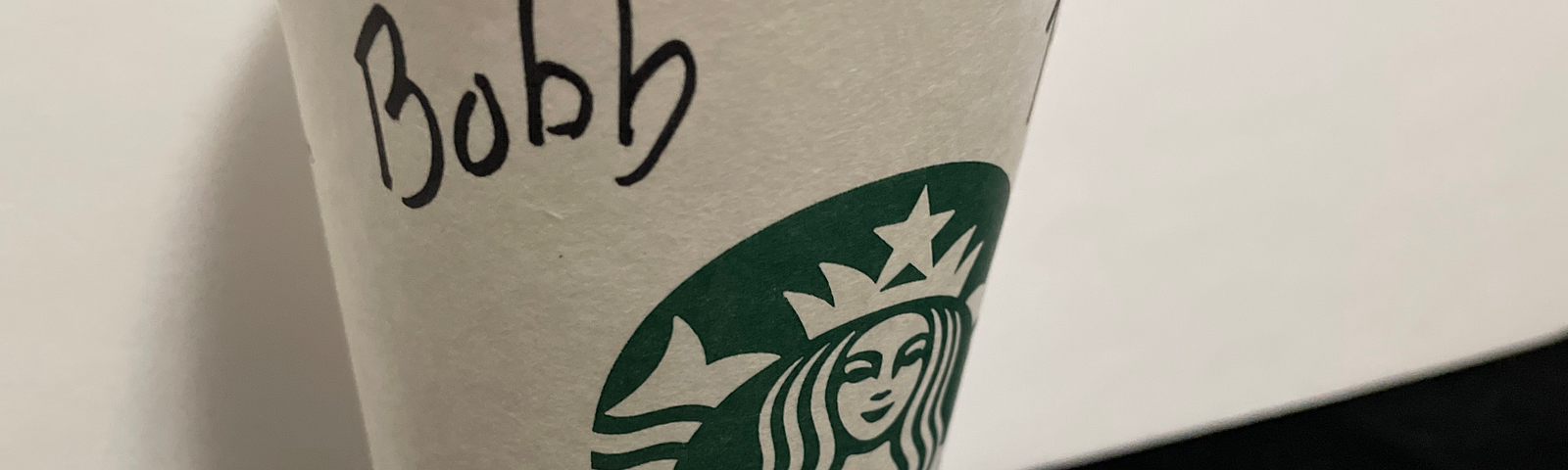 A Starbucks cup sits on a black counter. The name Bob (misspelled as “Bobb”) is written on it in black marker.