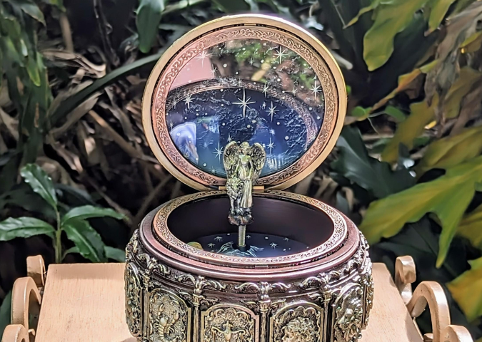 Picture of a beautiful music box engraved with the astrological signs in different shades of gold. Inside and in the lid is a deep blue with painted white stars. In the middle, is an angel with big wings, a lion at her side.