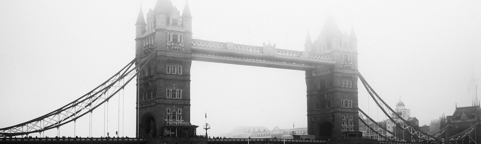 Eerie black and white picture of London bridge taken by the riverside on a foggy day.