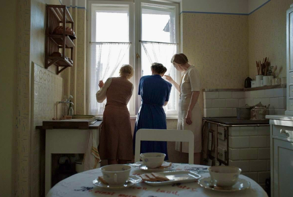 Three women look out the window to the camp next door. Zone of Interest movie, film review, critic, Best Picture, Oscar.