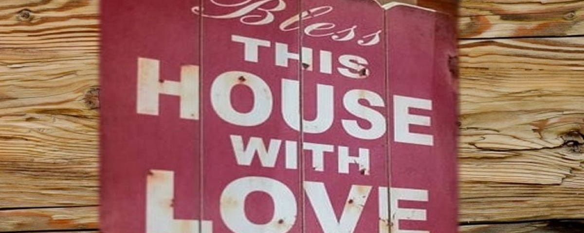 A red sign that reads, “Bless this house with love and laughter” hands against a wood grain backdrop.