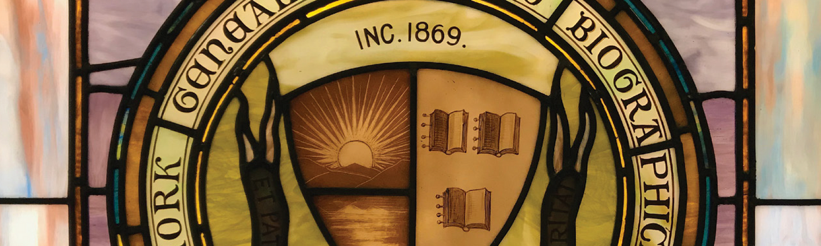 A stained glass window depicting the seal of the New York Genealogical and Biographical Society. The seal is divided in half, consisting of a rising sun over water on the left and three open books on the right.