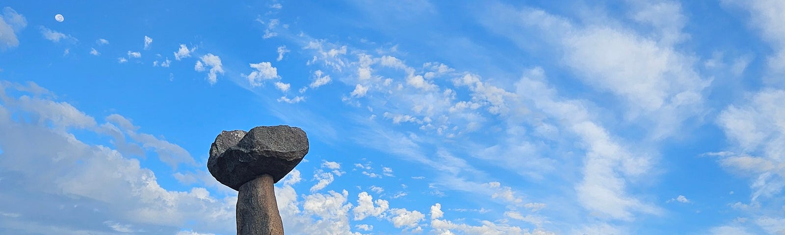 tall 14 foot natural stone pillar with a round cap, placed beside a 5 foot horizontal stone which is supported by two natural uprights. Overlook a beach horizon