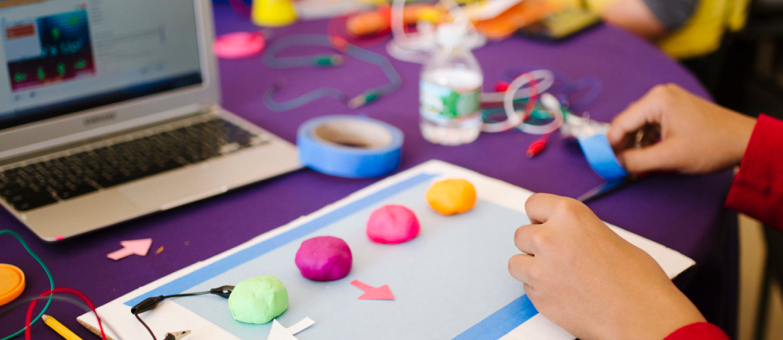 View of a child’s hands as they work on hands-on learning projects while guided by an online tutorial.