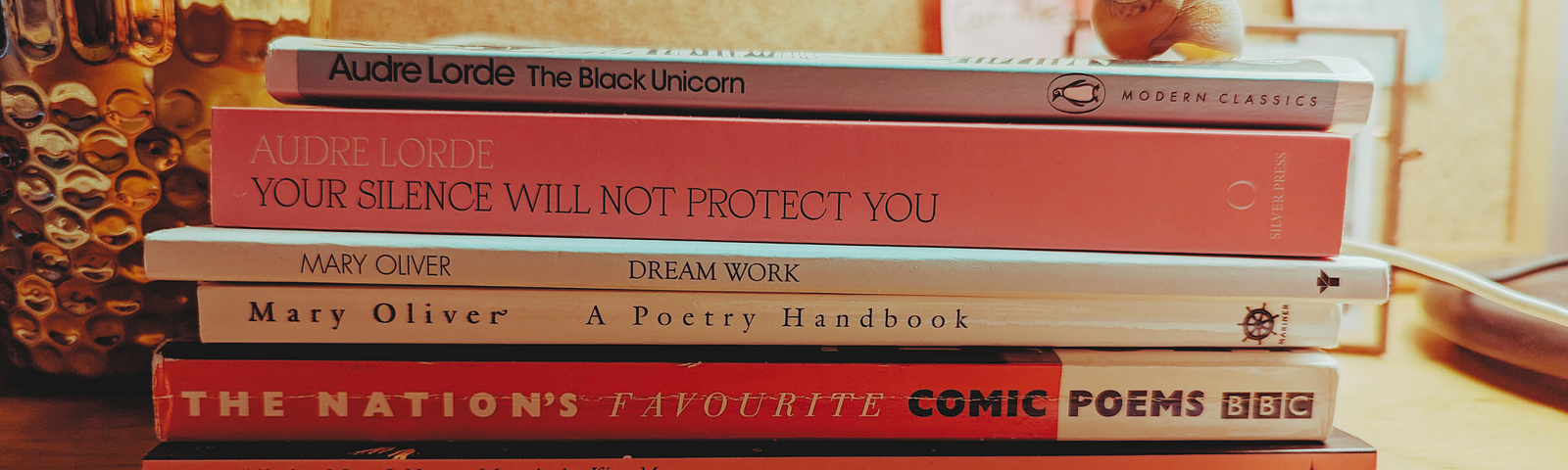 A stack of books on a desk. From bottom to top: The English Summer; All the Ment I Never Married; The Nation’s Favourite Comic Poems; A Poetry Handbook; Dream Work; Your Silence Will Not Protect You; The Black Unicorn