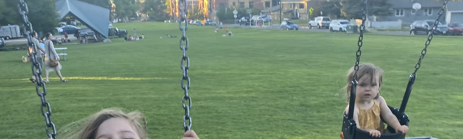 My toddler girls swing at a playground with mountains in the backdrop.